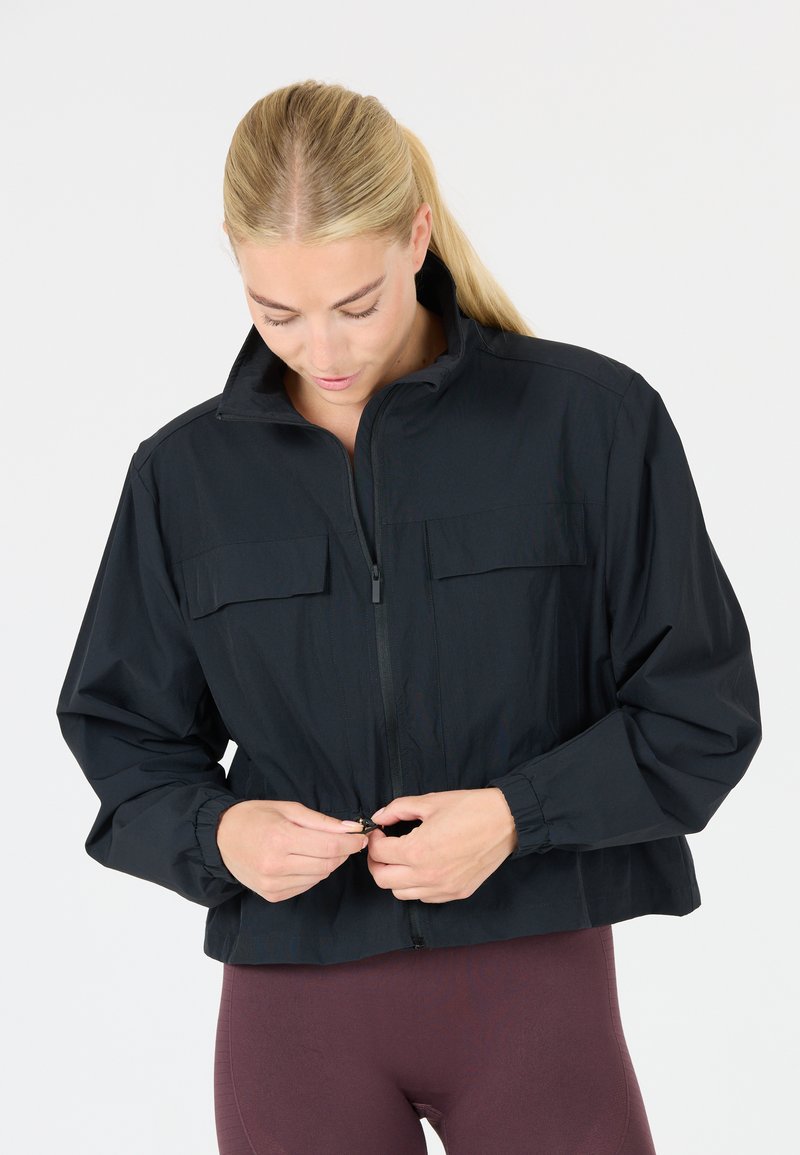 Black cropped jacket with a high collar, two front pockets, and elastic cuffs. The fabric appears lightweight and smooth, with a zip closure.
