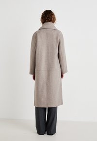 Beige ullblandingsjakke med bred krage, rett skjæring og synlige sømdetaljer. Bært over grå bukser.
