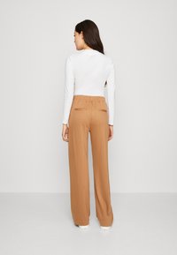 Pantalons à jambe large de couleur brun clair avec des rayures verticales, ceinture élastique et deux poches arrière, associés à un haut ajusté à manches longues blanc.