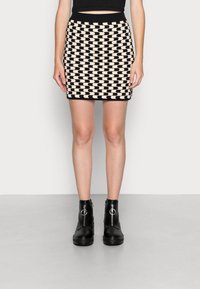 Schwarzer und cremefarbener Minirock mit Muster und geripptem Bund, kombiniert mit schwarzen Stiefeletten mit Reißverschluss und Ringdetail.