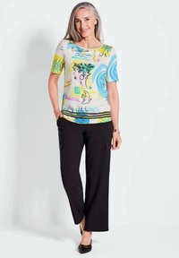 Bunt gemusterte Kurzarmbluse mit abstrakten Designs in Gelb, Blau und Pink, kombiniert mit schwarzen weiten Hosen und schwarzen Schuhen.