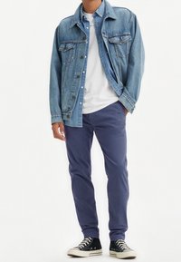 Světlá modrá džínová bunda přes bílé tričko, doplněná tmavě modrými kalhotami a černými teniskami s vysokou špičkou. Má kapsy na knoflíky a viditelné švy.