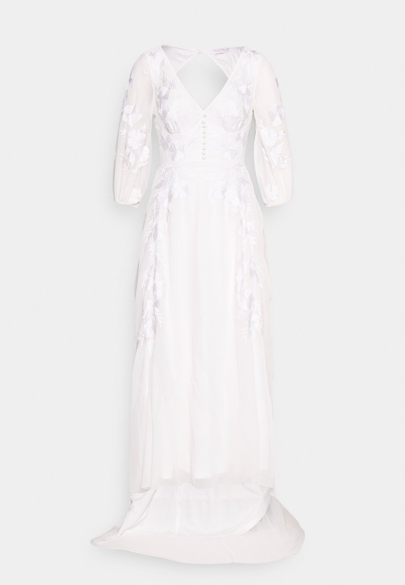 Robe de mariée blanche à manches longues avec broderie florale, corsage boutonné, décolleté en V et traîne fluide.