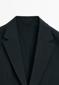 Schwarzer Blazer mit strukturiertem Kragen, glatter Textur und taillierten Revers. Das Design konzentriert sich auf klare Linien und minimale Details.