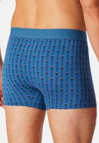 Blaue Boxer aus weichem Stoff mit einem wiederholenden Muster aus schmalen vertikalen Linien und kleinen Akzenten in dunklen und hellen Farben.