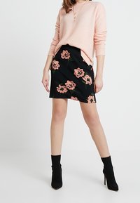 Rosa tröja med långa ärmar, kombinerad med en svart blommig kjol med rosa blommor. Modellen har på sig svarta klackboots.