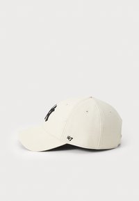 Cream-colored cap with a black logo on the front, structured design, curved visor, six panels, and embroidered accents on the side.