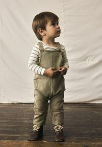 Pantalones de mezclilla verdes con bolsillos y botones de madera, combinados con una camisa de rayas de manga larga y zapatos marrones. Diseño sencillo, textura suave.
