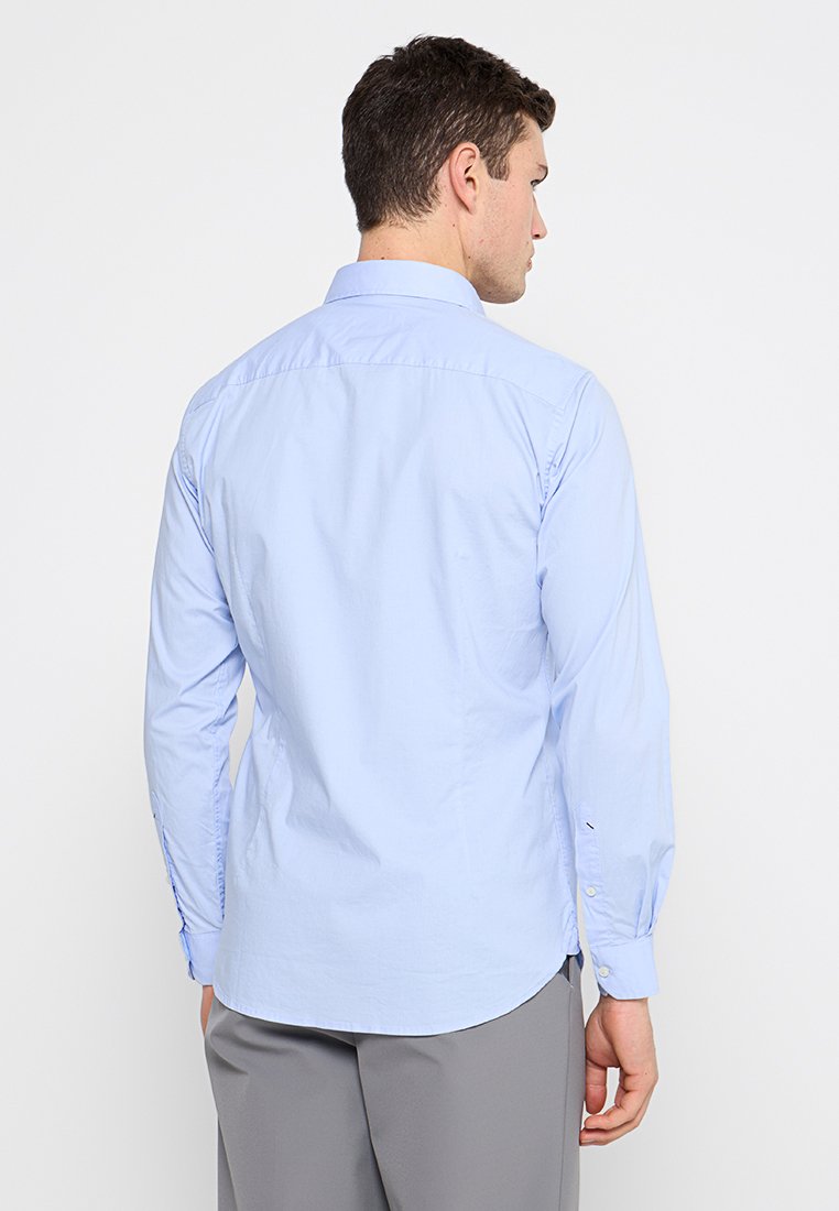 Camicia a maniche lunghe azzurro chiaro in cotone, con colletto standard, polsini con bottone e orlo diritto. Dettagli di cucitura visibili sulle maniche.
