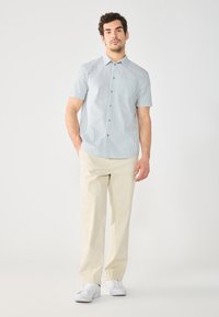 Chemise à manches courtes avec des rayures verticales bleues et blanches, col boutonné, et pantalons beiges, assortis à des baskets blanches.