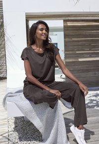 Dark brown, short-sleeve top with a relaxed fit and matching pants. White sneakers and a light gray textured blanket draped over a bench.