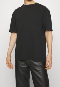 Černé bavlněné tričko s volným střihem, kulatým výstřihem a krátkými rukávy; má jemné švy a hladkou strukturu.