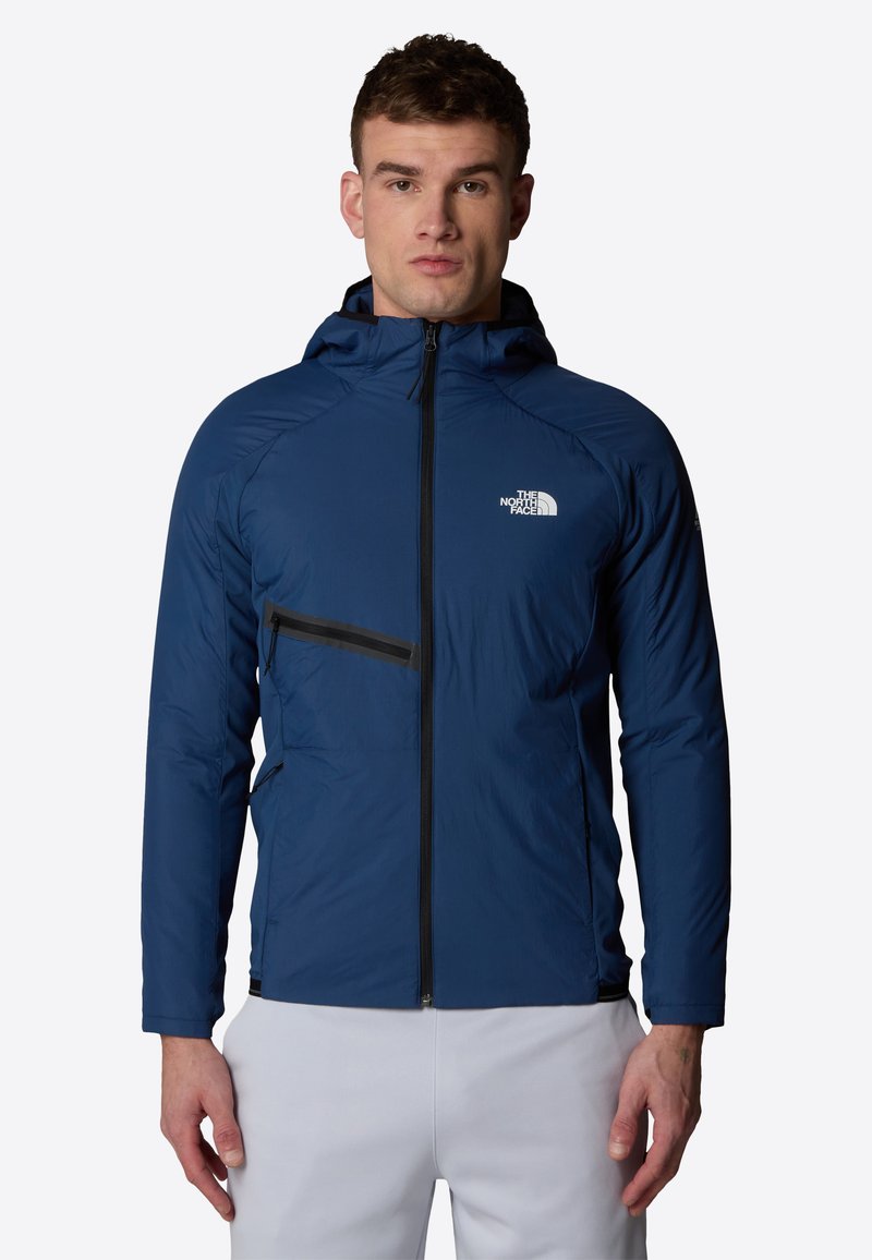 Blå lättviktsjacka med dragkedja fram, sidofickor och huva. Har svarta accenter och en logotyp på bröstområdet.