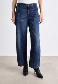 Weite, dunkelblaue Denim-Jeans mit hoher Taille, ausgestattet mit einem Knopf- und Reißverschluss, subtilen Ausbleichungen und gestickten Saumdetails.