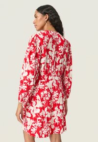 Vestido floral rojo con patrones blancos, mangas largas, cintura fruncida para dar estructura y textura de tela suave.