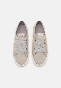 Baskets en toile grise à surface texturée, dotées de lacets plats passant par des œillets dorés et d'une semelle en caoutchouc blanche. Étiquette de marque visible à l'intérieur.