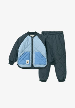 Costum două piese matlasat în nuanțe de bleumarin închis și albastru deschis, având o jachetă cu fermoar și buzunare contrastante, precum și pantaloni cu talie elastică.