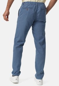 Herren-Hose in Hellblau mit Streifen, elastischem Bund, seitlichen Taschen und lockerem Schnitt, kombiniert mit weißen Turnschuhen.