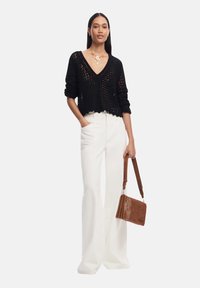 Maglione cropped nero a maglia con scollatura a V, abbinato a pantaloni bianchi a gamba larga. Accessoriato con una borsa a spalla marrone.