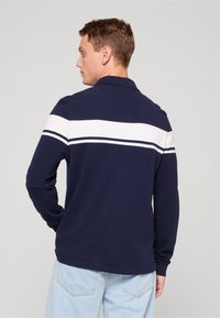 Námornícka dlhá polokošeľa s bielym vodorovným pásom cez hornú časť chrbta. Mäkká tkanina, golierový dizajn a voľný strih.