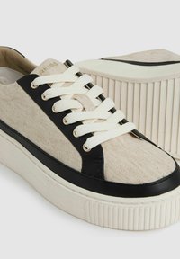 Canvas en leren sneakers met een beige bovenwerk, zwarte accenten en witte veters. Dikke, gestructureerde rubberen zool met verticale groeven.