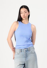 Svetlo modra rebrasta majica brez rokavov s prilegnjenim krojem, okroglo izrezom in širšimi naramnicami, v kombinaciji z visokim pasom svetlih jeansov.