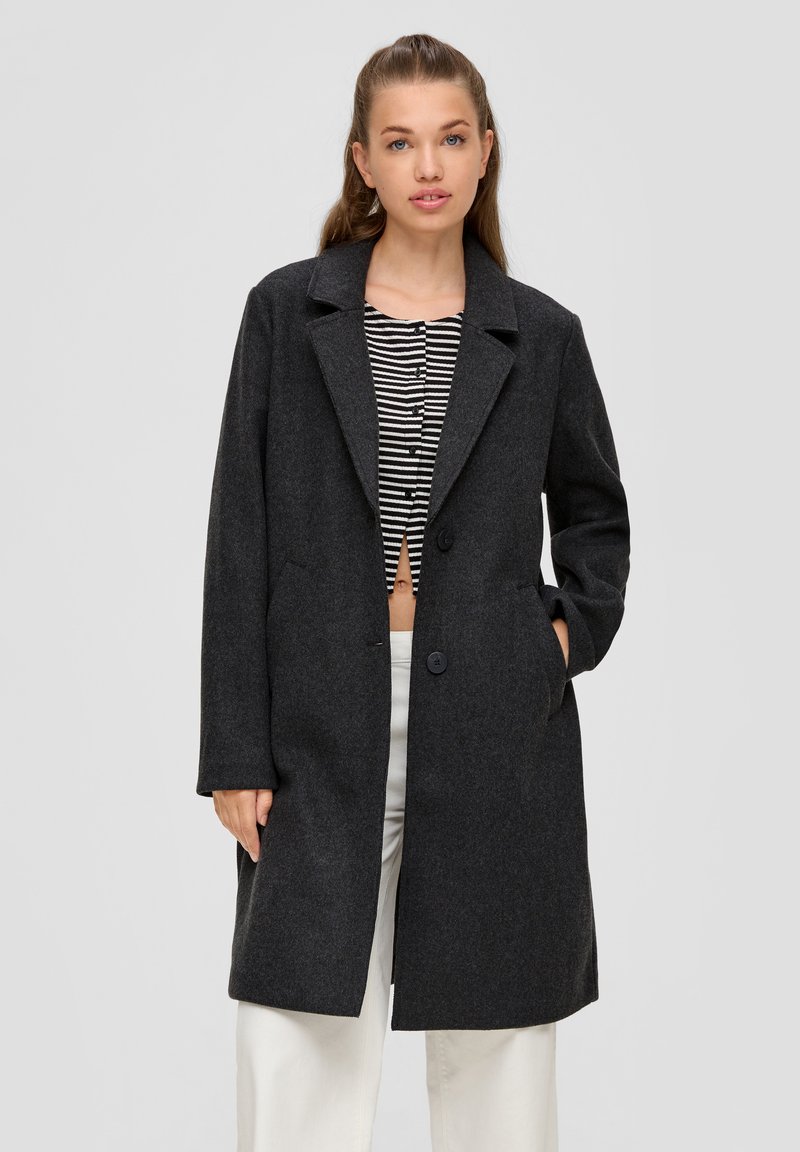 Grau melierter Wollmischmantel mit Reverskragen, zwei Knöpfen und seitlichen Taschen. Getragen über einem gestreiften Cropped-Top mit langen Ärmeln.