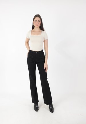 Top beige de cuello cuadrado y mangas cortas, combinado con pantalones de tiro alto negros y botas de tobillo negras de punta afilada. Diseño simplista.