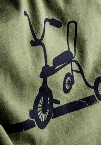 Groene stof toont een zwarte silhouet van een driewieler, die zijn wielen, handgrepen en zitting weergeeft in een minimalistisch ontwerp.