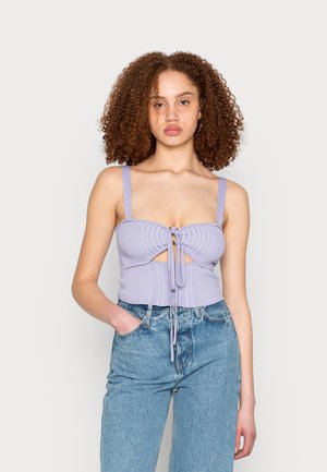 Camisola curta em lilás com nervuras, frente ajustável com laço, recortes e alças largas; combinada com jeans de ganga de cintura alta em azul claro.