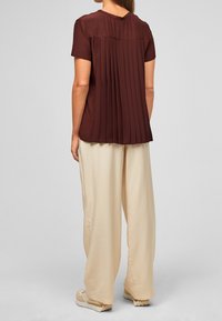 Blouse bordeaux à manches courtes avec un dos plissé, assortie à un pantalon beige ample, offrant une coupe décontractée et une texture douce.