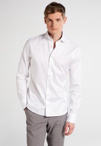 Weißes Button-Up-Hemd mit langen Ärmeln, taillierte Passform, aus weichem Baumwollstoff und klassischem Kragen. Die Knöpfe sind hellbraun und bieten einen subtilen Kontrast.