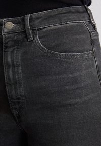 Czarne dżinsy w denimie o dopasowanym kroju, subtelnym przetarciu i klasycznym pięciokieszeniowym stylu z srebrnymi akcentami.