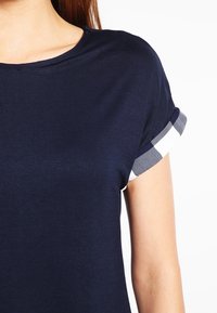 Mörkblå t-shirt med kort ärm, prydd med ett rutigt mönster på de rullade ärmsluten. Tillverkad av mjukt, andningsbart tyg.