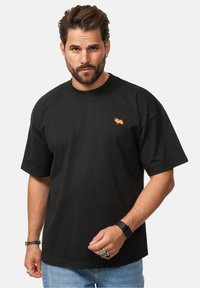 Black cotton t-shirt with a crew neck, featuring a small colorful embroidered design on the chest. Short sleeves and relaxed fit.