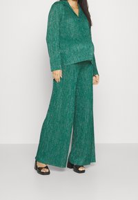 Grön glittrig stickad tvådelad outfit som består av en långärmad skjorta med krage och vida byxor, parat med svarta platåsandaler.