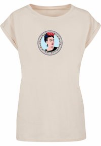 Beige bomulds t-shirt med en cirkulær grafisk tryk af en kvinde med blomster i håret, omgivet af en dekorativ blomsterkant.