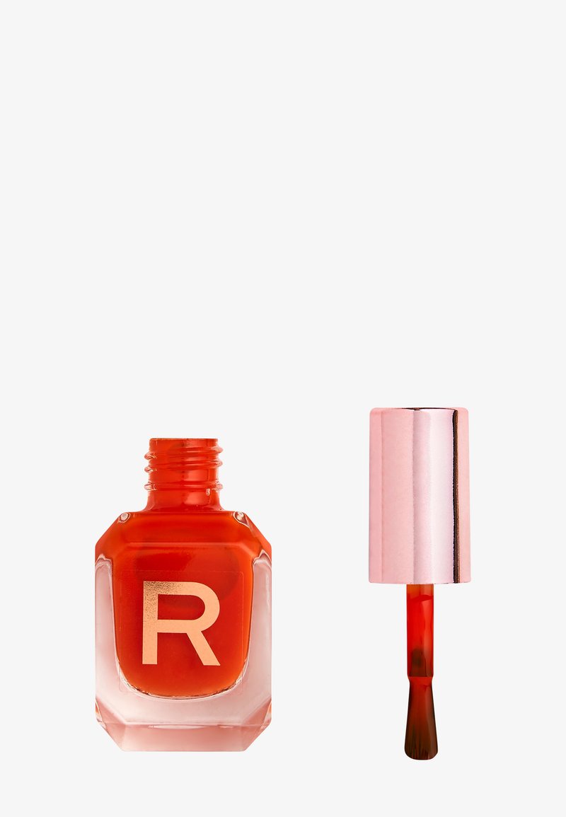 Open bottle of red nail polish with a rose gold cap and brush applicator beside it on a white background.