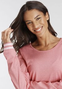 Langarmshirt in Hellrosa mit einem runden Ausschnitt und weißen gestreiften Akzenten an den Ärmeln. Weicher Stoff, lockerer Schnitt.