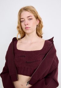 Pulôver cropped em bordeaux com tecido texturizado, apresentando um decote quadrado e detalhe de logotipo. Combinado com uma hoodie bordeaux com fecho de correr.
