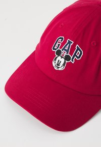 Casquette de baseball rouge en coton avec un texte "GAP" brodé et un design de Mickey Mouse à l'avant. Visière incurvée avec un tissu texturé.