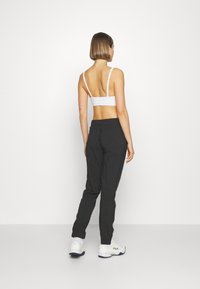 Balta sporta bralette un melnas šauras bikses. Tērps ir ar regulējamiem siksnām, elastīgu jostu un gludu tekstūru.