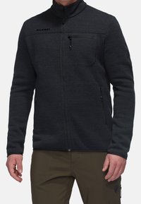 Giacca in pile nera con colletto alto, zip frontale, tasca con zip sul petto e tasche laterali, caratterizzata da una finitura texturizzata e dettaglio del logo.