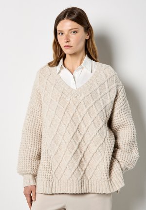 Cremfarbener, gestrickter Pullover mit einem strukturierten Rautenmuster und gerippten Bündchen. V-Ausschnitt und lockere Passform. Aus reinem Wolle material.