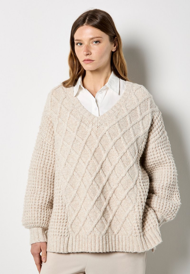 Cremfarbener, gestrickter Pullover mit einem strukturierten Rautenmuster und gerippten Bündchen. V-Ausschnitt und lockere Passform. Aus reinem Wolle material.