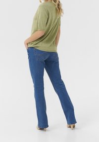 Olivgrön kortärmad topp med texturerade prickar, kombinerad med blå denimjeans med vinklade bakfickor och slim fit.