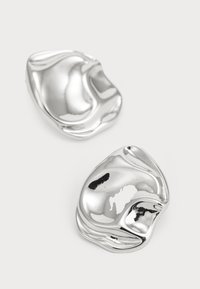 Boutons de manchette en métal argenté avec un design lisse et ondulé. La surface polie réfléchit la lumière, mettant en avant des formes organiques et des contours subtils.