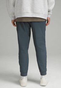 Ciemnoszare spodnie sportowe o tapered fit, z prążkowanymi mankietami na kostkach i gładką fakturą materiału, noszone z jasnoszarym oversized swetrem.