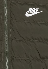 Dunkelolivgrüne Steppjacke mit horizontalen Nähten, vorn mit Reißverschluss und weißem Nike-Logo auf der oberen linken Seite.
