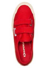 Baskets en toile rouges avec deux bandes Velcro, semelle en caoutchouc beige, surface texturée et étiquette blanche sur le côté.